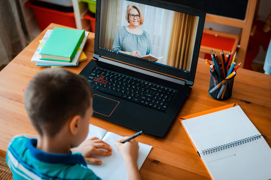A student takes notes while watching an online teacher on a laptop